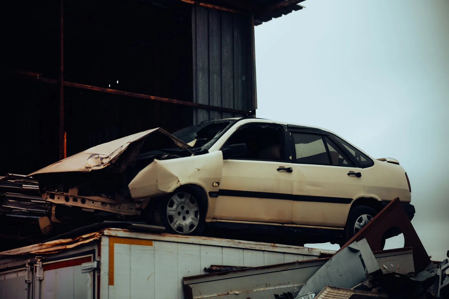 A crashed cream sedan sitting on top of a heap of scrap metal