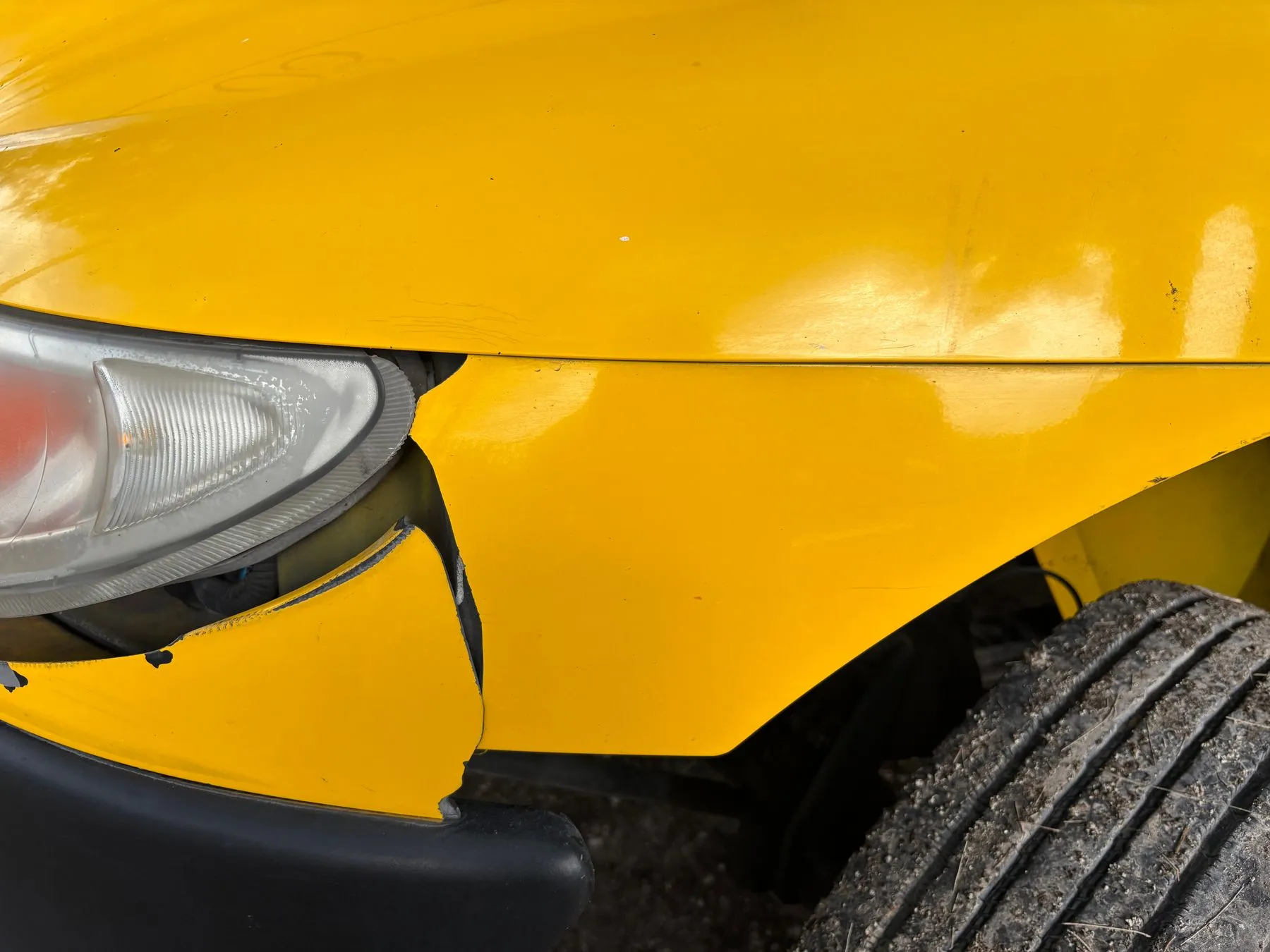 Close view of a yellow car with a crushed front bumper and a broken headlight