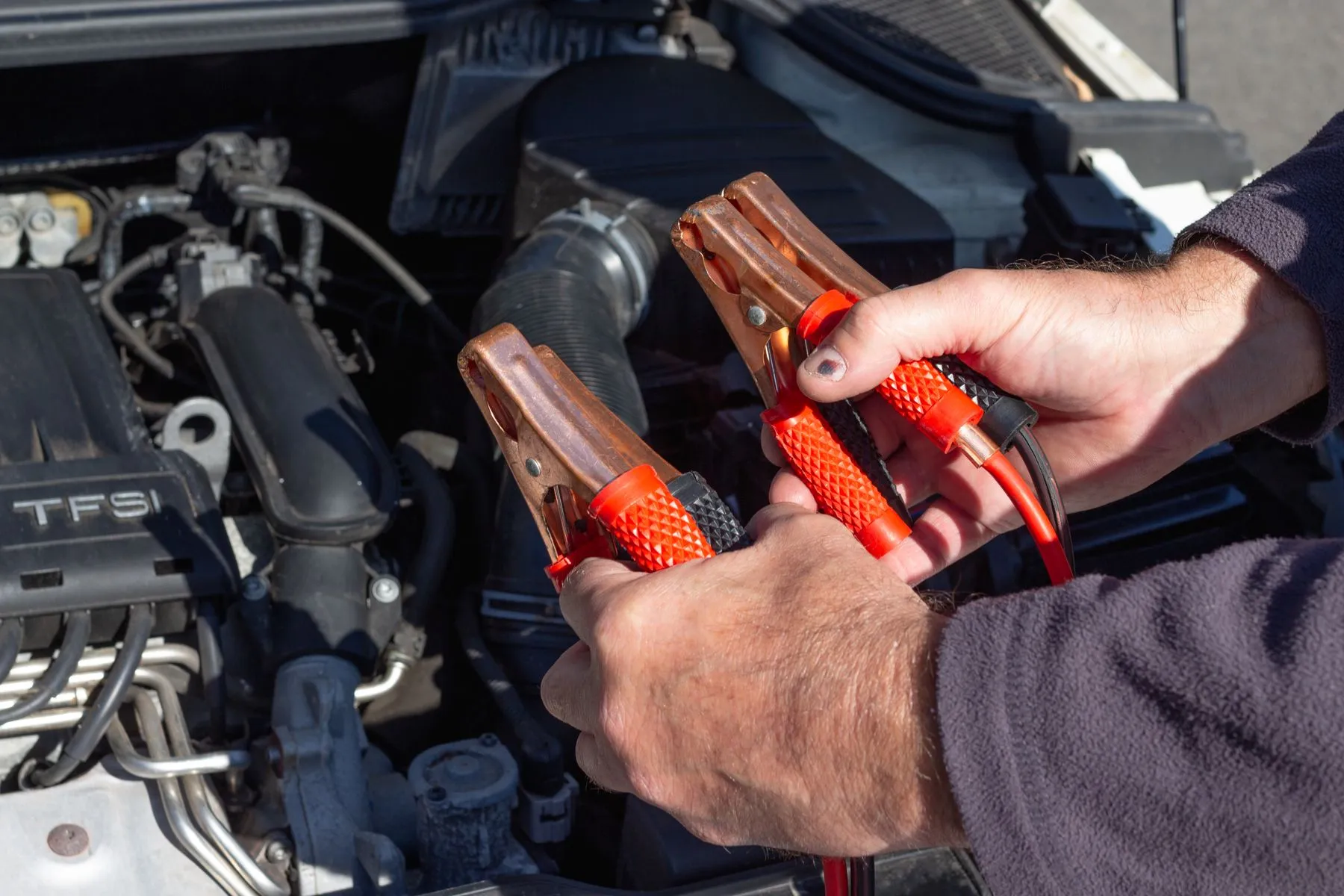 Hands holding jumper cable clamps over an open car engine bay