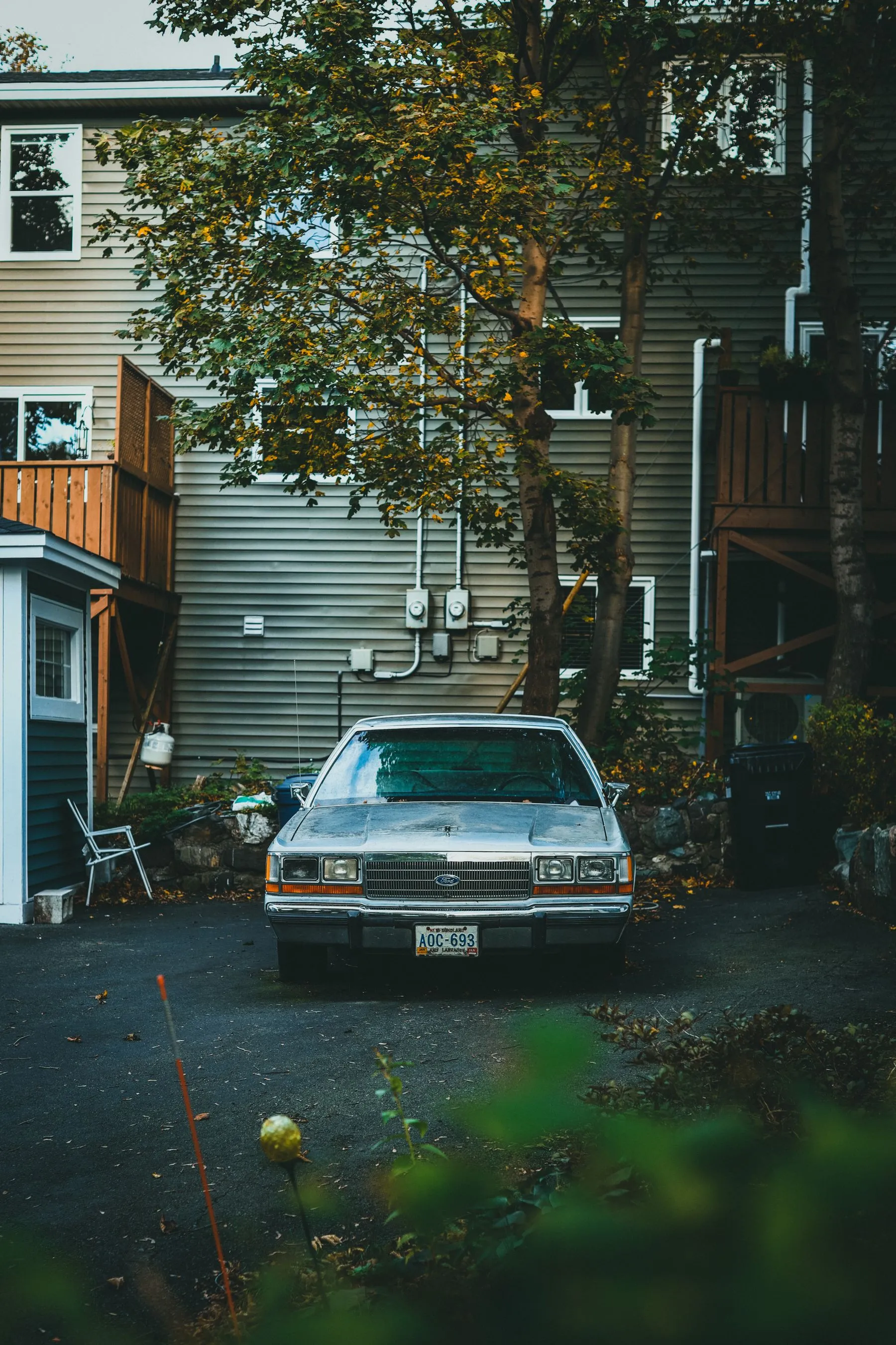 An old silver sedan parked in front of a house among autumn trees