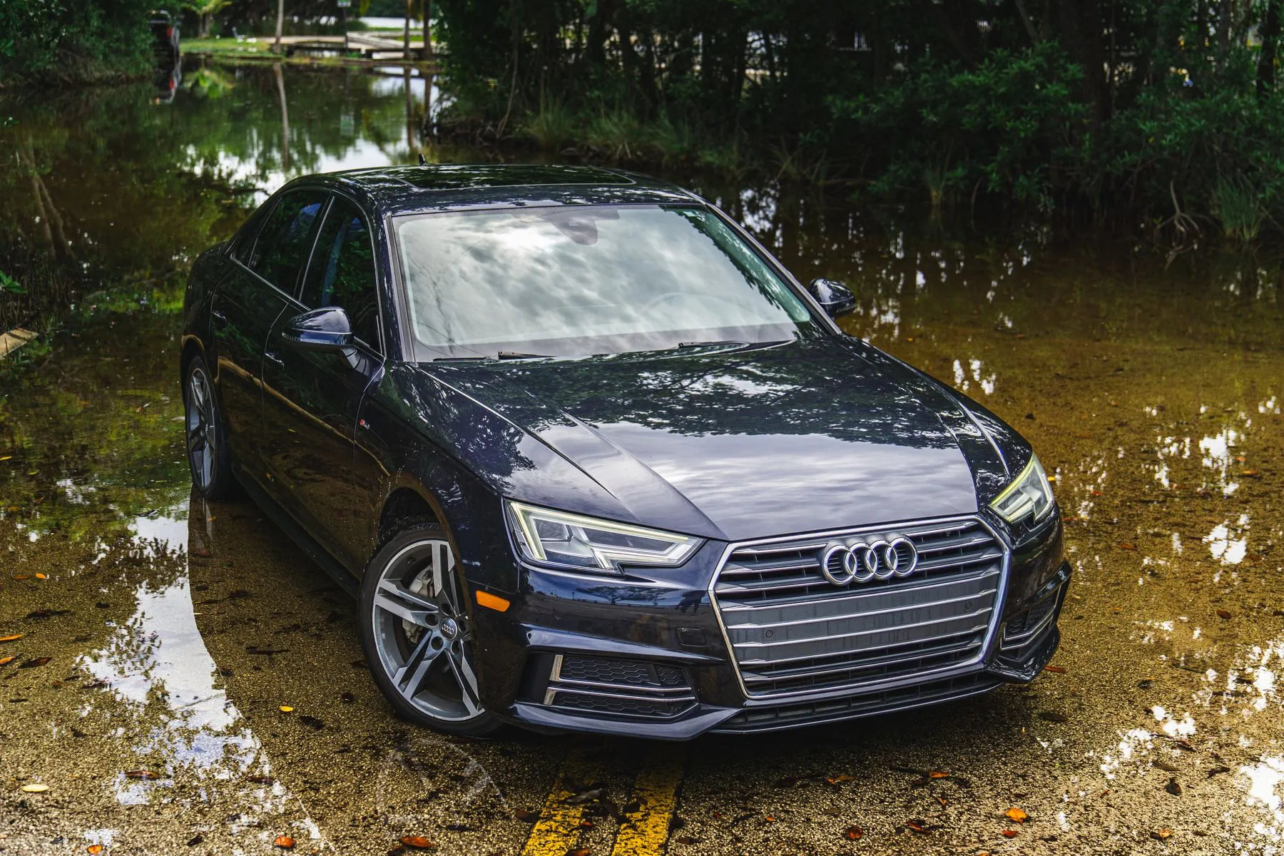 A dark sedan sitting on a flooded road with water around its wheels