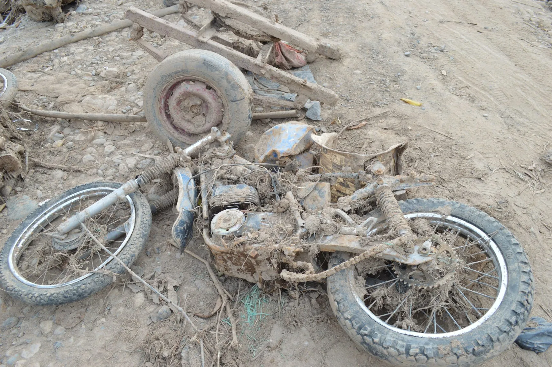 A wrecked motorcycle lying on its side in dirt and debris, its frame bent and parts scattered